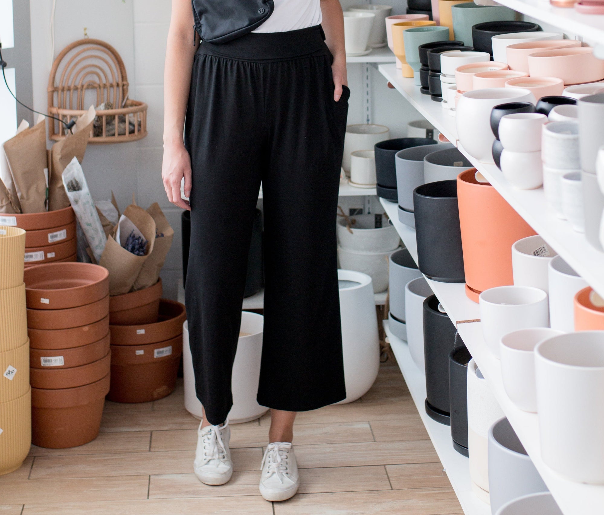 woman wearing white t shirt and black wide leg pants standing in a room with plant pots