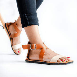 Female model in black jeans wearing the Brave Soles sustainably made Jasmine leather sandals with recycled tire soles in ivory and caramel colour