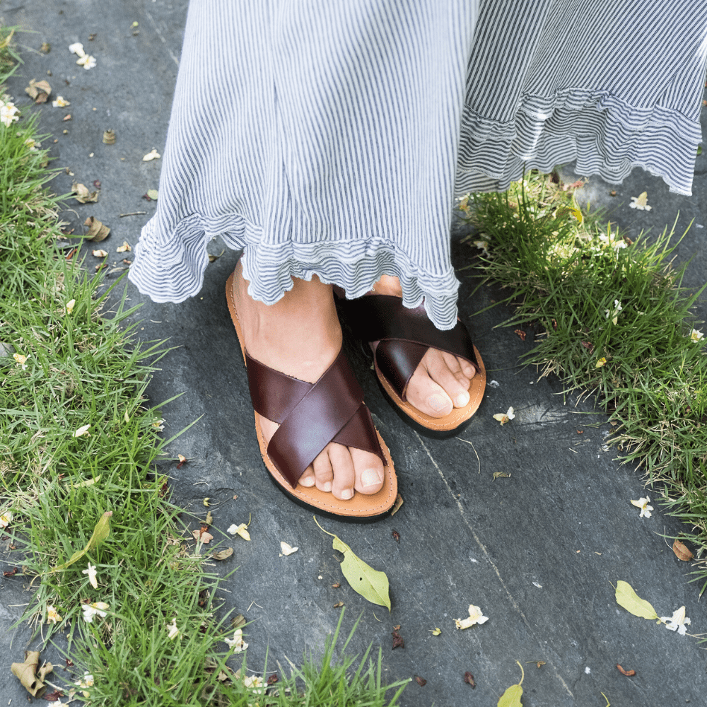 Front side view of the Brave Soles Constanza leather slide sandal that is sustainably made and has upcycled tire soles. Pictured in root beer and natural color.