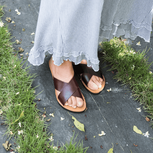 Female model in long, flowing skirt wearing the Brave Soles Constanza leather slide sandal that is sustainably made and has upcycled tire soles. Pictured in root beer and natural color.