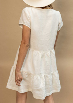 Backside of the Elwood Mini Dress in Coconut which is a beautiful linen in ivory. The model is shot in studio and wears a white wide brim hat. Effortless minimal pieces to live in your wardrobe for many years.