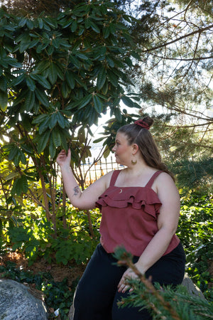 woman sitting by a tree wearing a soft red tank top with ruffles