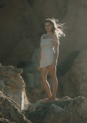 The Mallee linen Romper with adjustable tie-up straps seen at the beach accessorized with pearls as the wind blows in our models hair in Australia. Simplistic and minimalist design to last you forever.