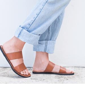 Female model wearing jeans with the Sustainably crafted Ophelia leather slide sandals from Brave Soles in caramel color.