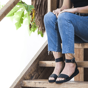 Female model sitting on steps and wearing a mid calf length dress with the Camila Flatform leather sandals sustainably made by Brave Soles in Classic Black.