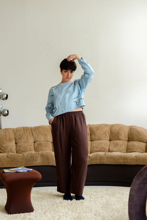 non-binary model wearing loose wide leg brown silky pants and a light blue top