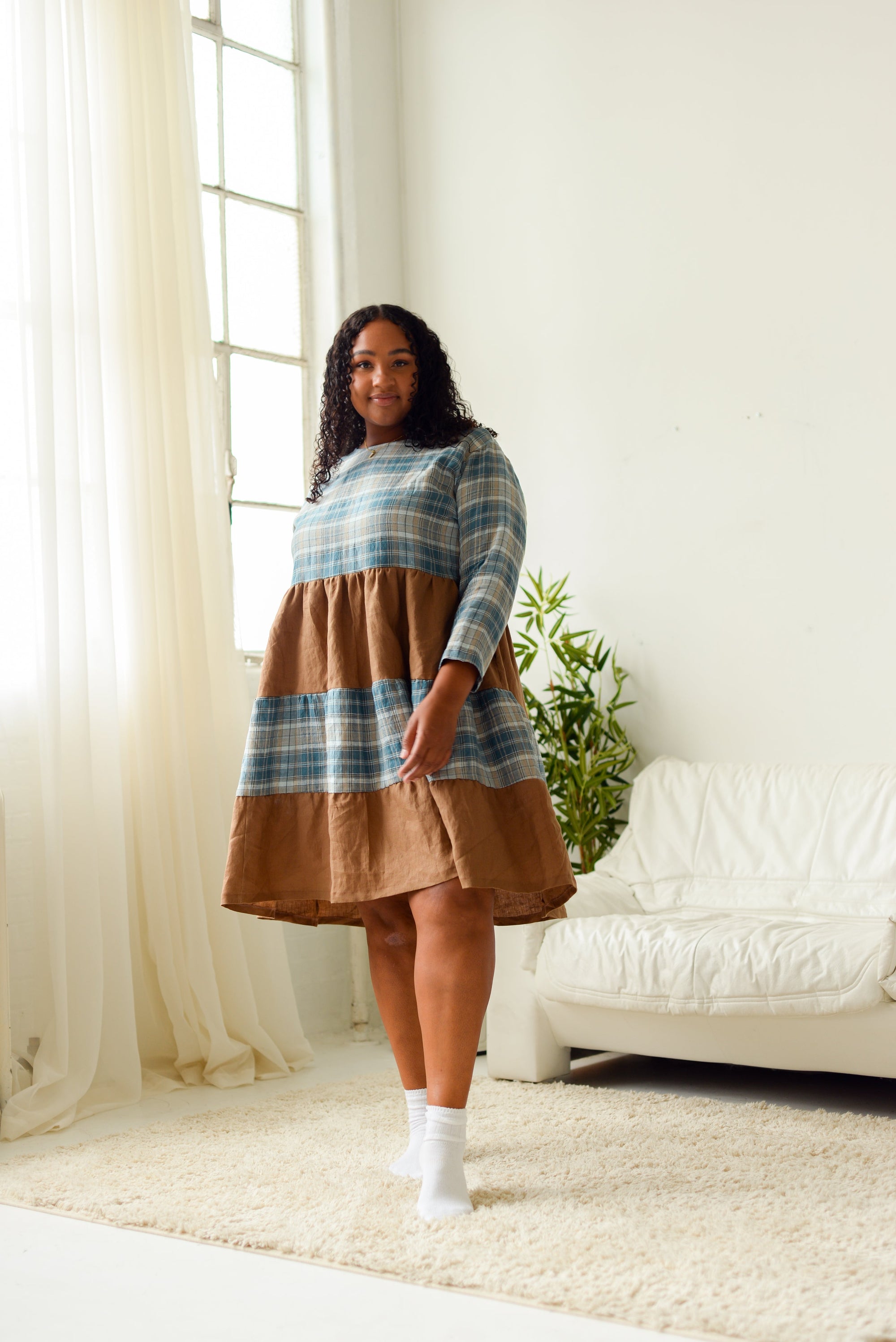 non-binary model wearing a teal plaid and brown tiered long sleeve loose fitting dress